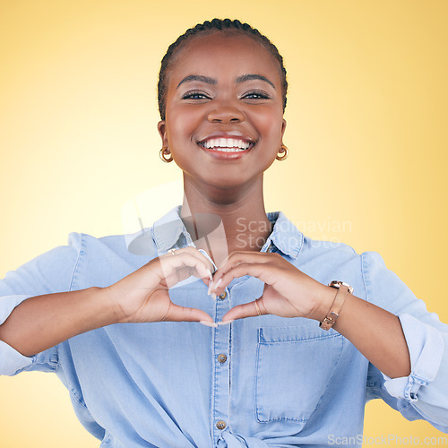 Image of Happy black woman, portrait and heart hands for love, care or support against a yellow studio background. Face of African female person smile with loving emoji, shape or symbol icon on valentines day