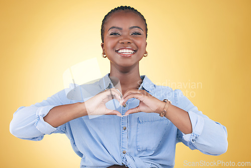 Image of Happy black woman, portrait and heart hands for support, love or care against a yellow studio background. Face of African female person smile with loving emoji, shape or symbol icon on valentines day