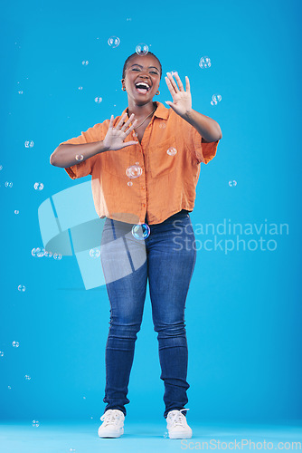 Image of Excited, happy and black woman on blue background with bubbles for happiness, joy and have fun. Playful, smile and isolated African person in studio with soap bubble for cheerful, magic and aesthetic