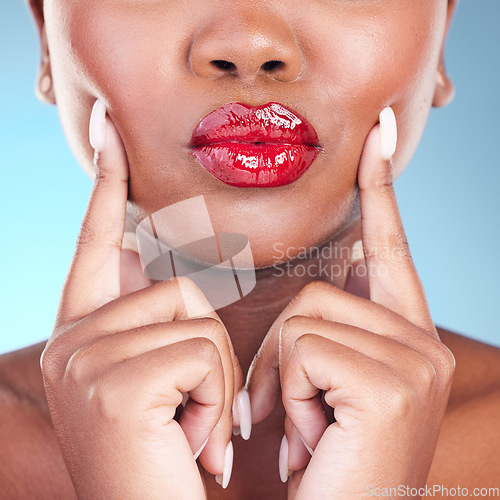 Image of Woman, kiss and red, lipstick and beauty, hands touching face and makeup closeup isolated on blue background. Model, bold and cosmetic product on lips, pout and mouth, manicure and shine in studio