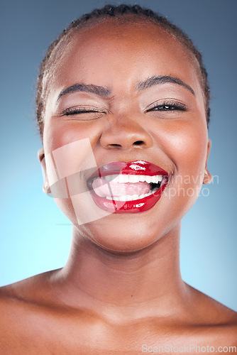 Image of Black woman, wink and flirt with red lipstick, beauty and makeup closeup with tongue out isolated on blue background. Model, bold and cosmetic product on lips, skin with shine and playful in studio