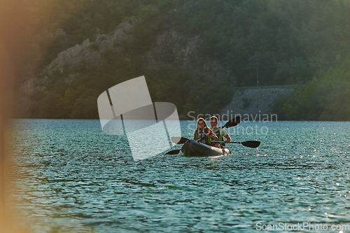 Image of A young couple enjoying an idyllic kayak ride in the middle of a beautiful river surrounded by forest greenery in sunset time