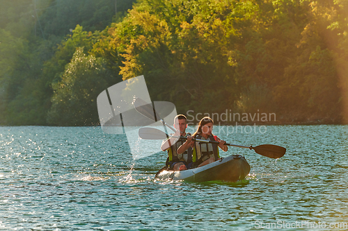 Image of A young couple enjoying an idyllic kayak ride in the middle of a beautiful river surrounded by forest greenery in sunset time