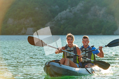 Image of A young couple enjoying an idyllic kayak ride in the middle of a beautiful river surrounded by forest greenery in sunset time