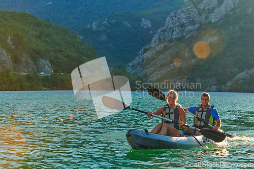 Image of A young couple enjoying an idyllic kayak ride in the middle of a beautiful river surrounded by forest greenery in sunset time