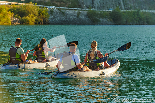 Image of A group of friends enjoying fun and kayaking exploring the calm river, surrounding forest and large natural river canyons during an idyllic sunset.