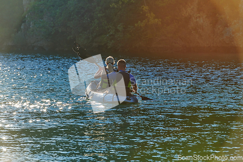 Image of A young couple enjoying an idyllic kayak ride in the middle of a beautiful river surrounded by forest greenery in sunset time