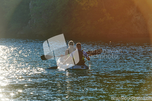 Image of A young couple enjoying an idyllic kayak ride in the middle of a beautiful river surrounded by forest greenery in sunset time