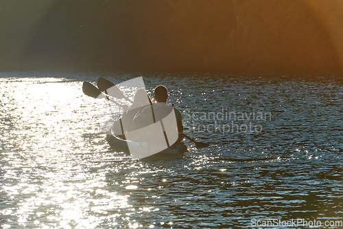 Image of A young couple enjoying an idyllic kayak ride in the middle of a beautiful river surrounded by forest greenery in sunset time