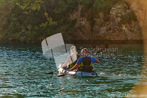 Image of A young couple enjoying an idyllic kayak ride in the middle of a beautiful river surrounded by forest greenery in sunset time