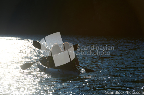 Image of A young couple enjoying an idyllic kayak ride in the middle of a beautiful river surrounded by forest greenery in sunset time