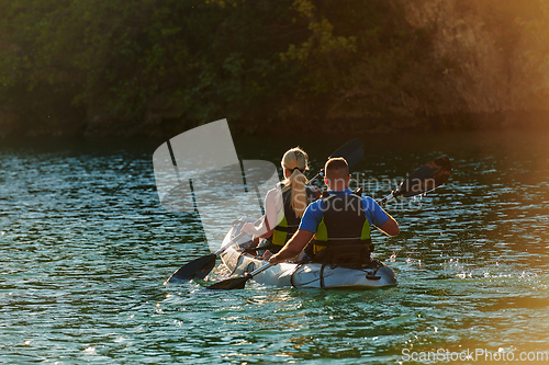 Image of A young couple enjoying an idyllic kayak ride in the middle of a beautiful river surrounded by forest greenery in sunset time