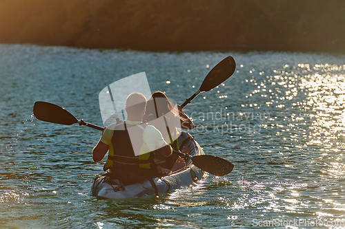 Image of A young couple enjoying an idyllic kayak ride in the middle of a beautiful river surrounded by forest greenery in sunset time