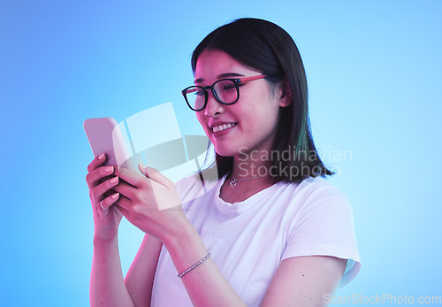 Image of Phone call, reading an Asian woman in conversation on mobile app to contact person online in studio blue background. Connection, cellphone and young female chatting with smile for communication