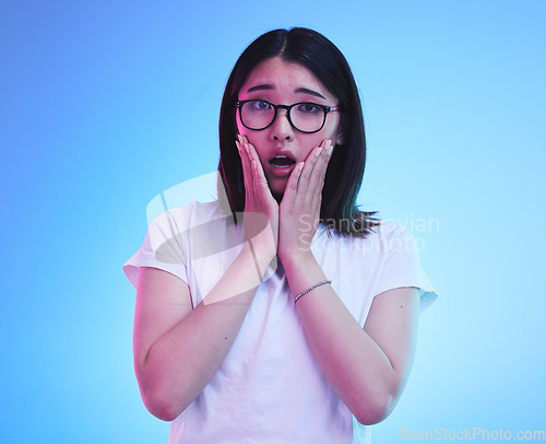 Image of Surprise, drama and face of Asian woman with fear expression, shocked or open mouth for crisis and fail. Omg, wtf and portrait of person with scared emoji isolated in a studio blue background