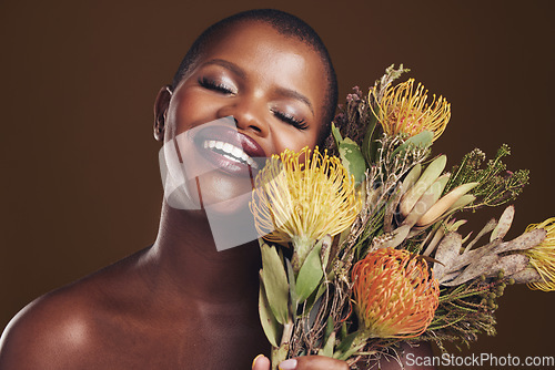 Image of Aesthetic, beauty and protea with the face of a black woman in studio on brown background for natural treatment. Smile, plant or cosmetics and a young model posing for skincare wellness with flowers