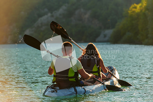 Image of A young couple enjoying an idyllic kayak ride in the middle of a beautiful river surrounded by forest greenery in sunset time