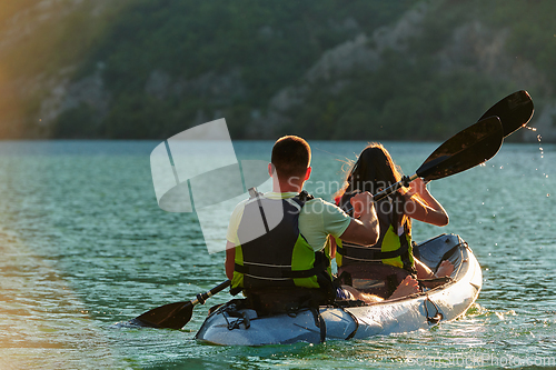 Image of A young couple enjoying an idyllic kayak ride in the middle of a beautiful river surrounded by forest greenery in sunset time