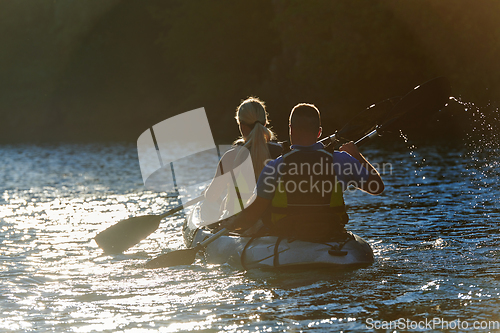 Image of A young couple enjoying an idyllic kayak ride in the middle of a beautiful river surrounded by forest greenery in sunset time