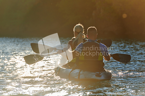 Image of A young couple enjoying an idyllic kayak ride in the middle of a beautiful river surrounded by forest greenery in sunset time