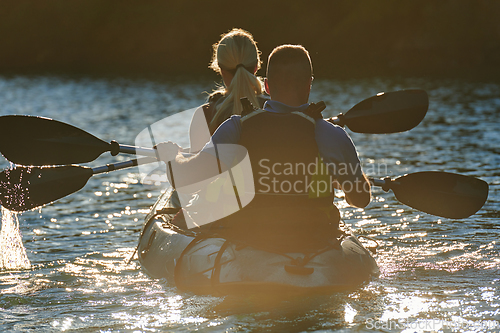 Image of A young couple enjoying an idyllic kayak ride in the middle of a beautiful river surrounded by forest greenery in sunset time