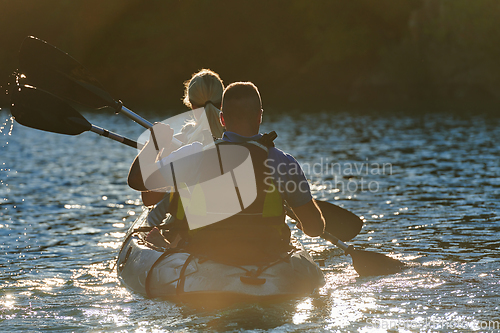 Image of A young couple enjoying an idyllic kayak ride in the middle of a beautiful river surrounded by forest greenery in sunset time