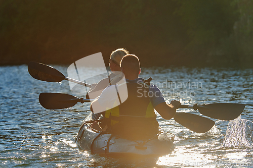 Image of A young couple enjoying an idyllic kayak ride in the middle of a beautiful river surrounded by forest greenery in sunset time