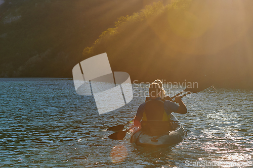 Image of A young couple enjoying an idyllic kayak ride in the middle of a beautiful river surrounded by forest greenery in sunset time