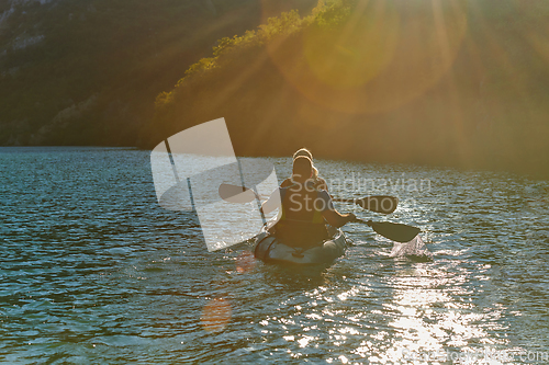 Image of A young couple enjoying an idyllic kayak ride in the middle of a beautiful river surrounded by forest greenery in sunset time