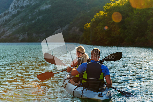 Image of A young couple enjoying an idyllic kayak ride in the middle of a beautiful river surrounded by forest greenery in sunset time