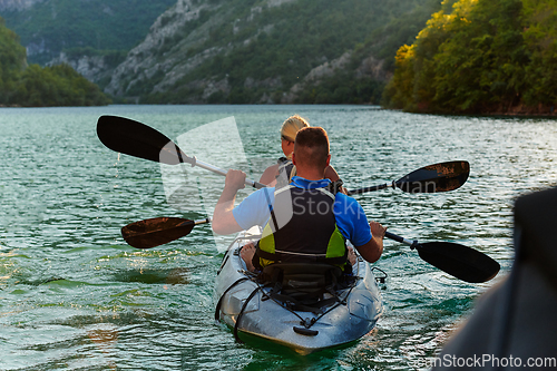 Image of A young couple enjoying an idyllic kayak ride in the middle of a beautiful river surrounded by forest greenery in sunset time