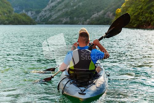 Image of A young couple enjoying an idyllic kayak ride in the middle of a beautiful river surrounded by forest greenery in sunset time