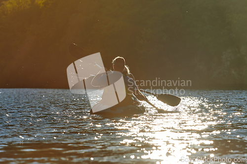 Image of A young couple enjoying an idyllic kayak ride in the middle of a beautiful river surrounded by forest greenery in sunset time