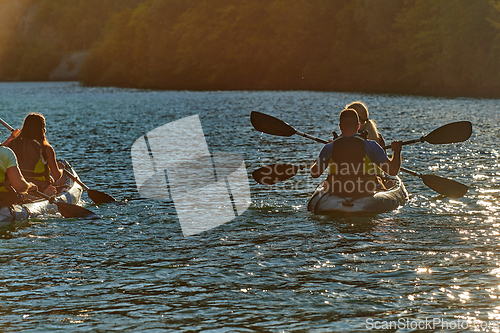 Image of A group of friends enjoying fun and kayaking exploring the calm river, surrounding forest and large natural river canyons during an idyllic sunset.