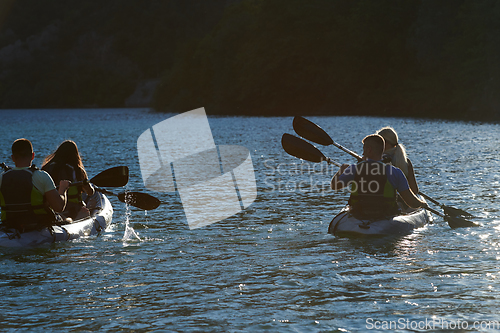 Image of A group of friends enjoying fun and kayaking exploring the calm river, surrounding forest and large natural river canyons during an idyllic sunset.