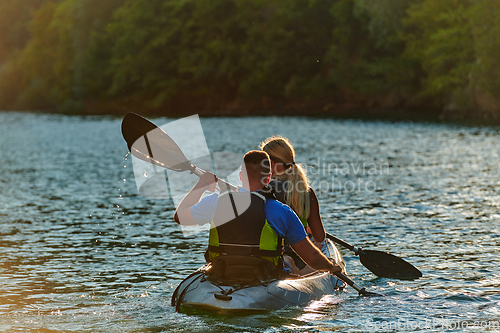 Image of A young couple enjoying an idyllic kayak ride in the middle of a beautiful river surrounded by forest greenery in sunset time