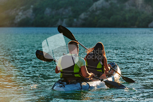 Image of A young couple enjoying an idyllic kayak ride in the middle of a beautiful river surrounded by forest greenery in sunset time