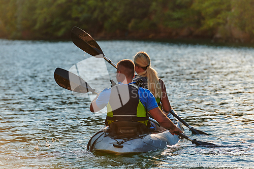 Image of A young couple enjoying an idyllic kayak ride in the middle of a beautiful river surrounded by forest greenery in sunset time