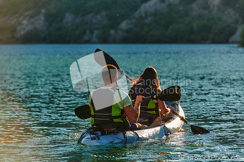 Image of A young couple enjoying an idyllic kayak ride in the middle of a beautiful river surrounded by forest greenery in sunset time