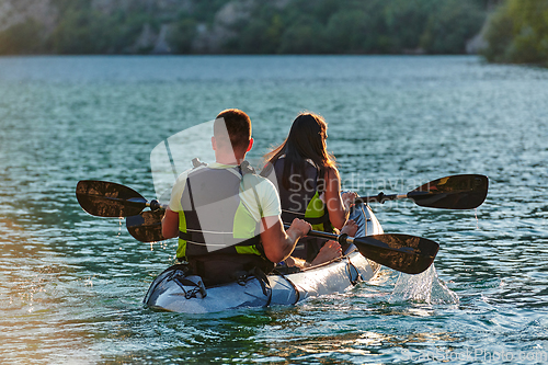 Image of A young couple enjoying an idyllic kayak ride in the middle of a beautiful river surrounded by forest greenery in sunset time