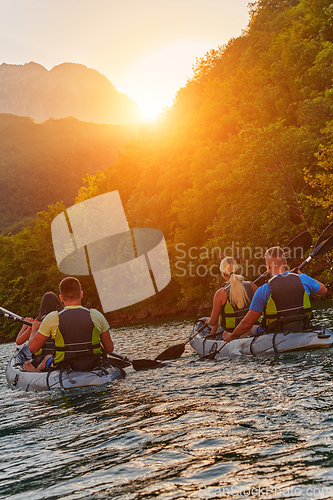 Image of A group of friends enjoying fun and kayaking exploring the calm river, surrounding forest and large natural river canyons during an idyllic sunset.