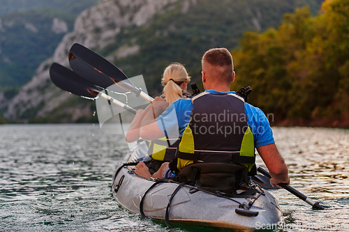 Image of A young couple enjoying an idyllic kayak ride in the middle of a beautiful river surrounded by forest greenery in sunset time
