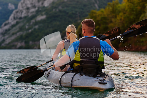 Image of A young couple enjoying an idyllic kayak ride in the middle of a beautiful river surrounded by forest greenery in sunset time