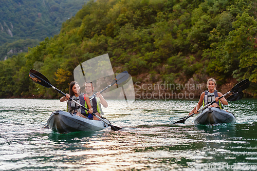 Image of A group of friends enjoying fun and kayaking exploring the calm river, surrounding forest and large natural river canyons during an idyllic sunset.