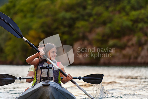 Image of A young couple enjoying an idyllic kayak ride in the middle of a beautiful river surrounded by forest greenery