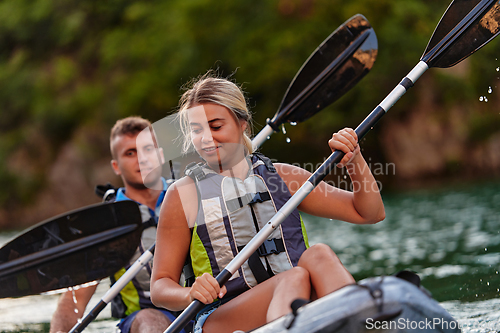 Image of A young couple enjoying an idyllic kayak ride in the middle of a beautiful river surrounded by forest greenery