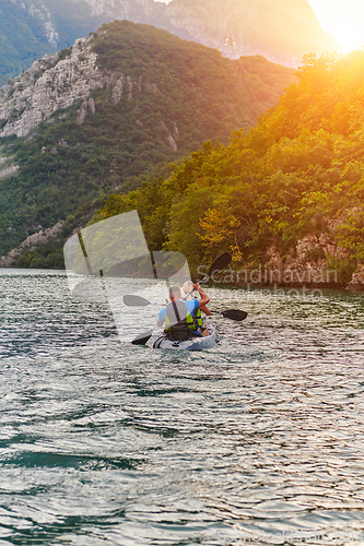 Image of A young couple enjoying an idyllic kayak ride in the middle of a beautiful river surrounded by forest greenery in sunset time