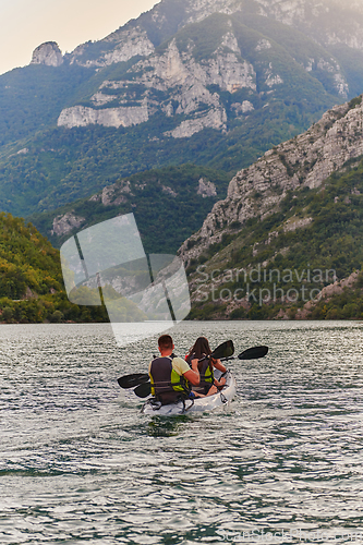 Image of A young couple enjoying an idyllic kayak ride in the middle of a beautiful river surrounded by forest greenery in sunset time