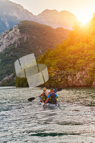 Image of A young couple enjoying an idyllic kayak ride in the middle of a beautiful river surrounded by forest greenery in sunset time