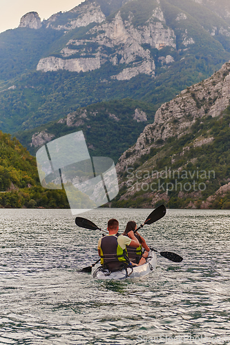 Image of A young couple enjoying an idyllic kayak ride in the middle of a beautiful river surrounded by forest greenery in sunset time